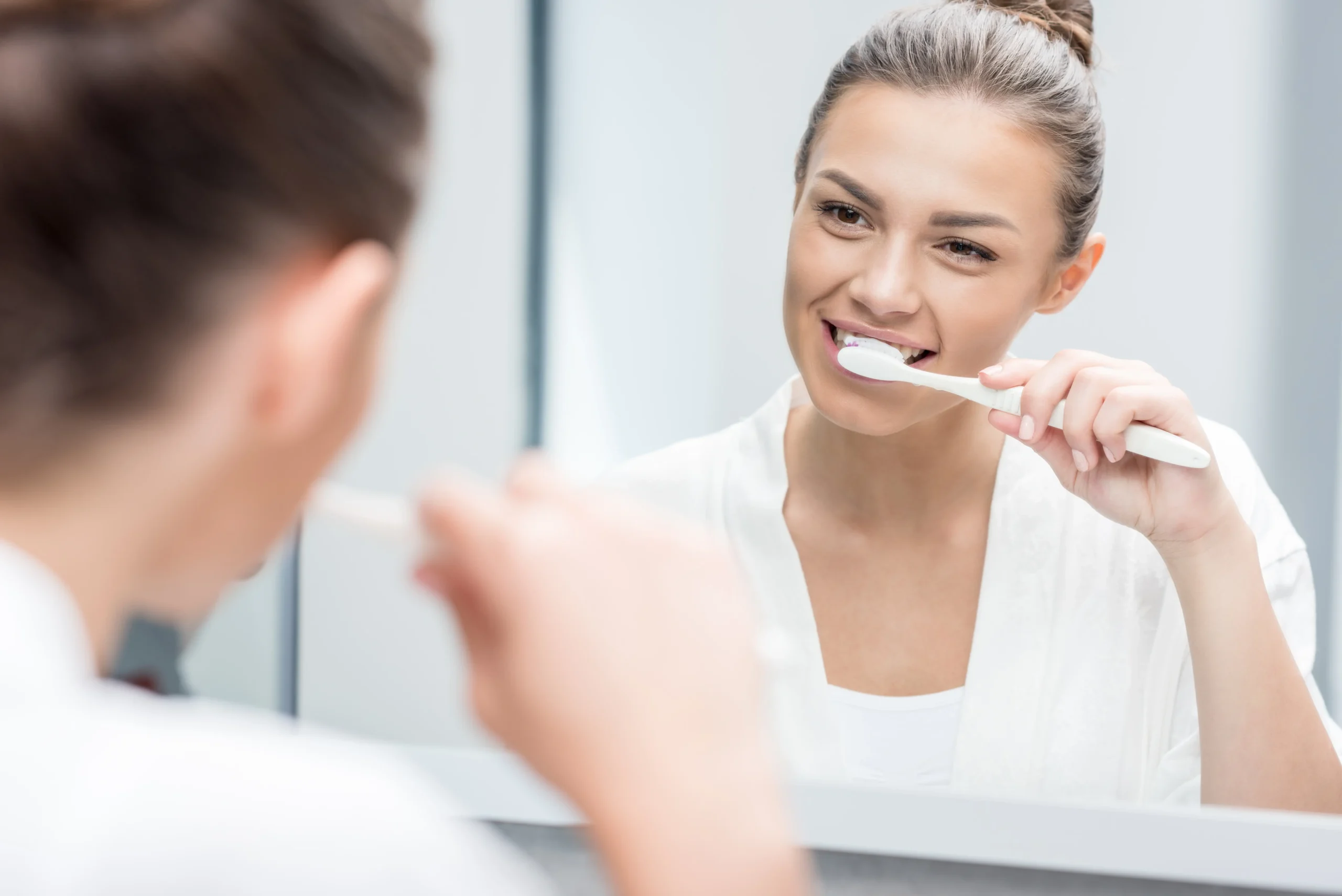 A young woman looking in the bathroom mirror brushing her teeth