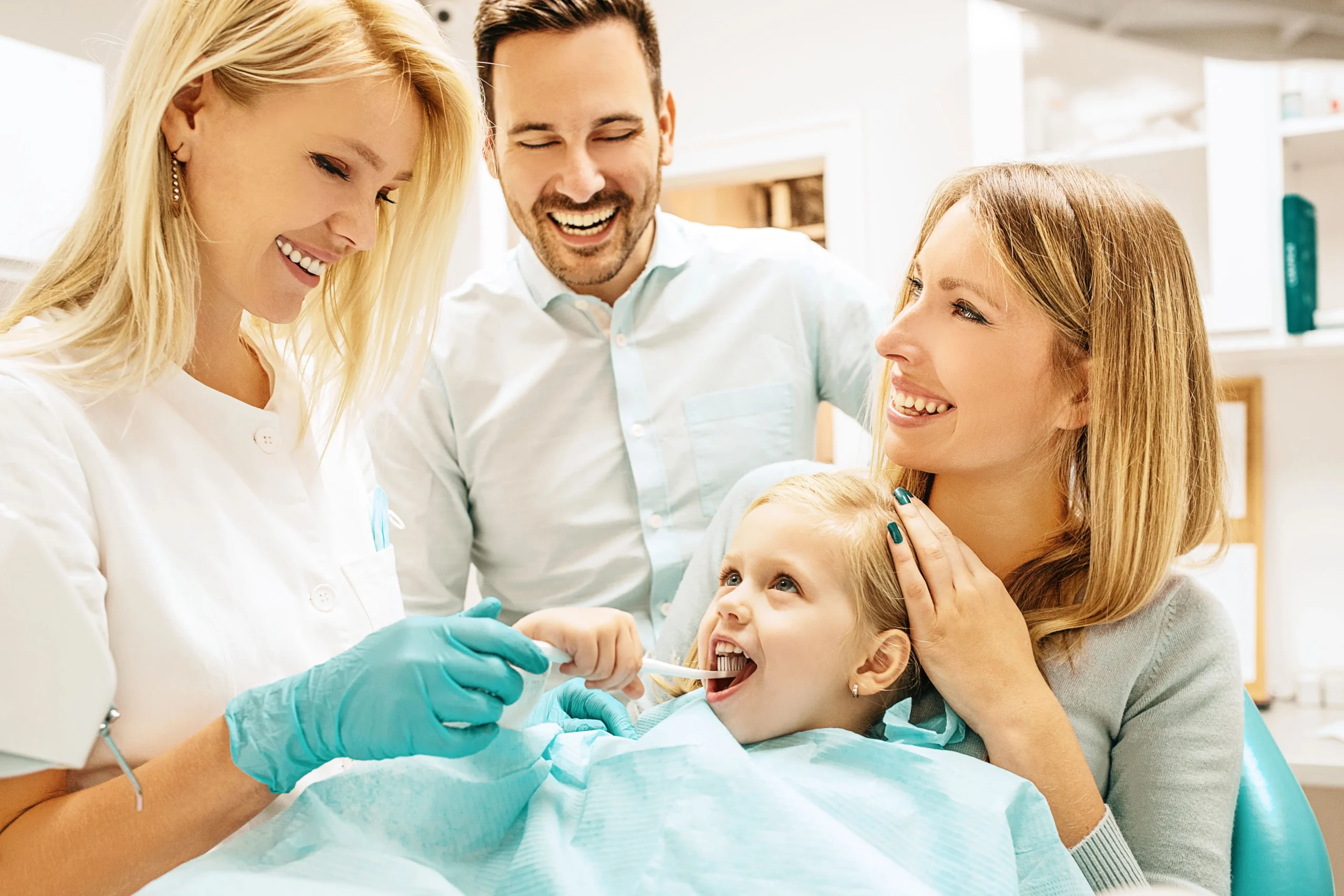 A dentist checking the teeth of a young patient while her parents look at her smiling.