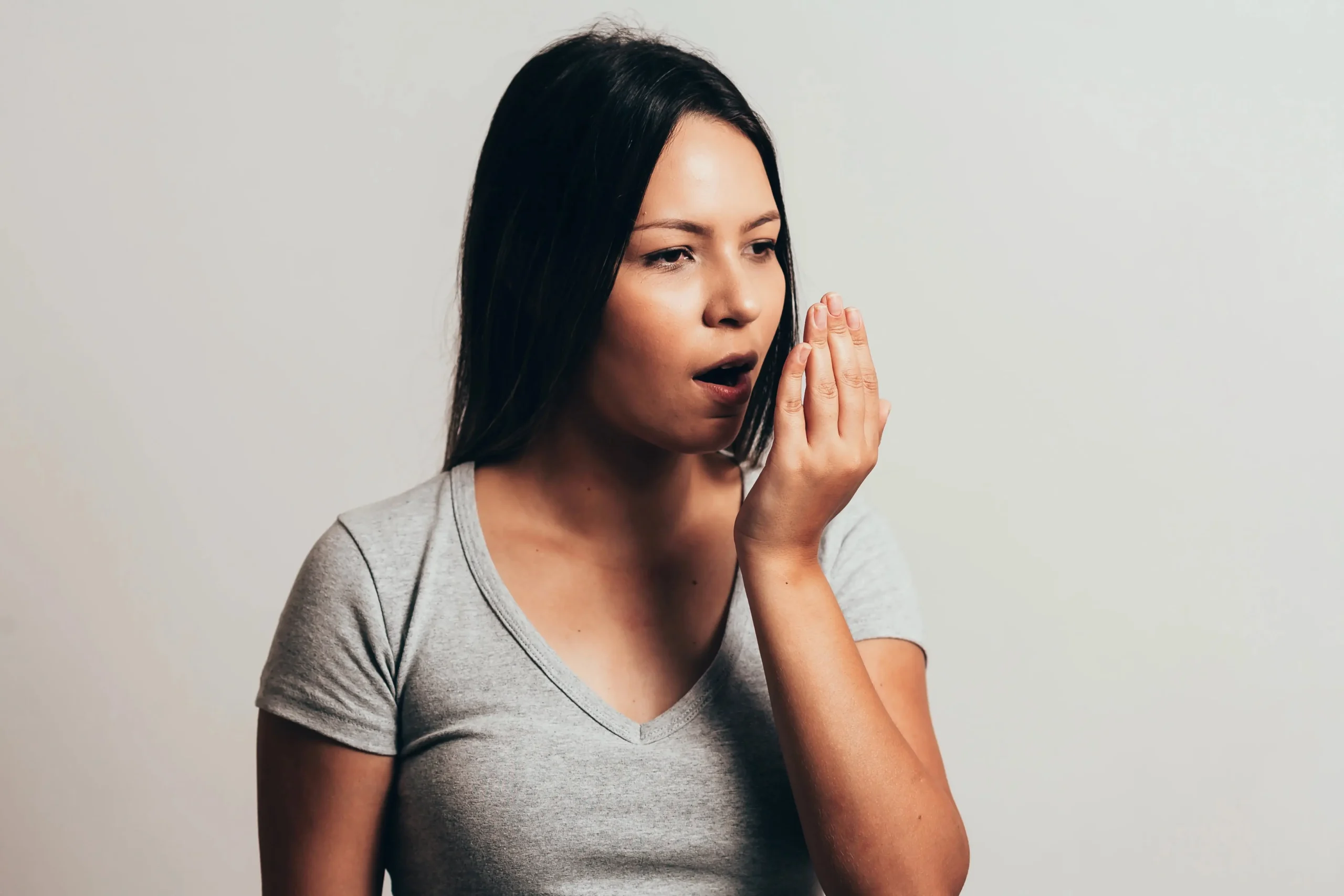 A woman with her hand to her mouth trying to smell her breath