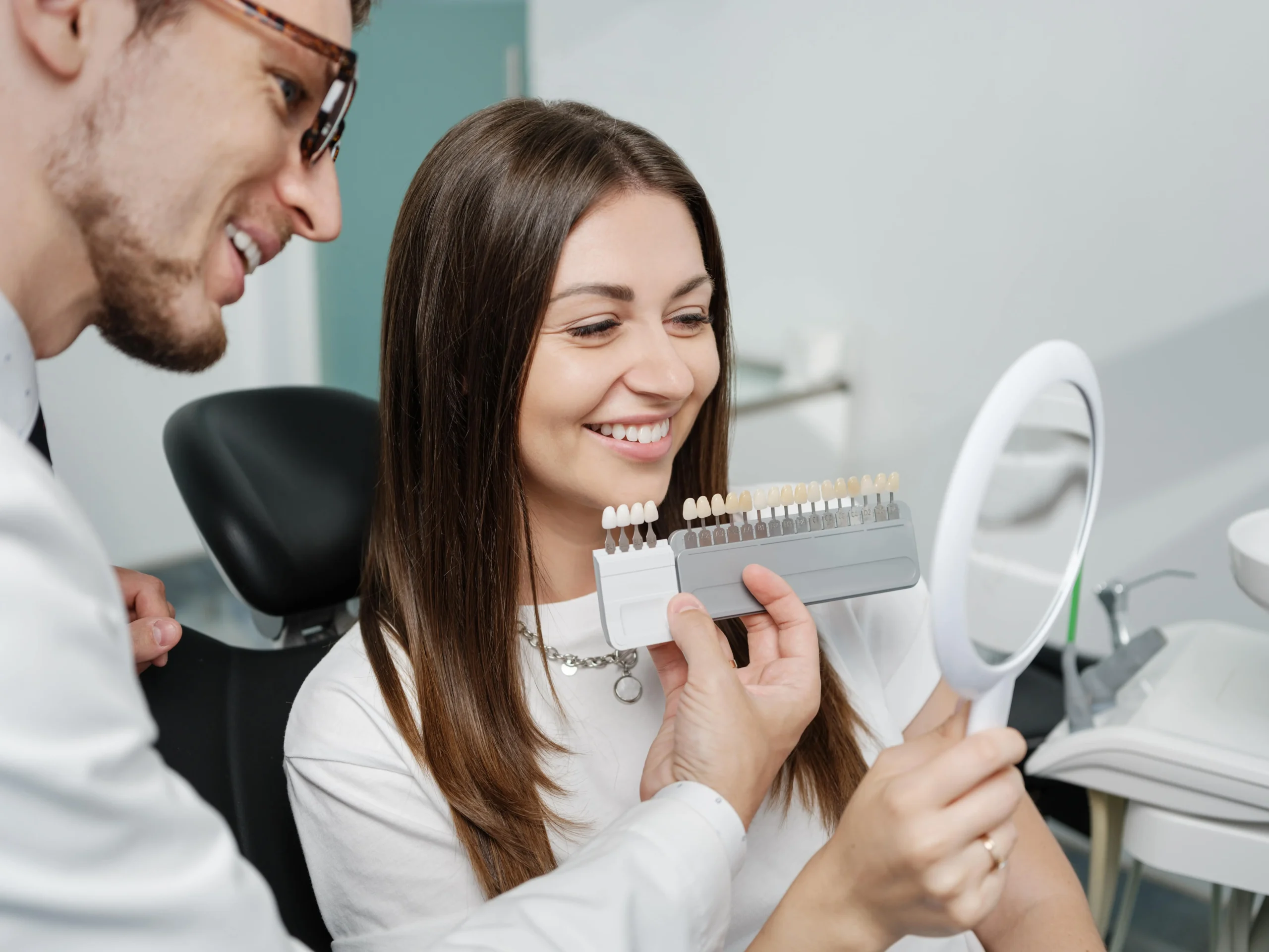 A woman seated on a dental chair looking at teeth shades.