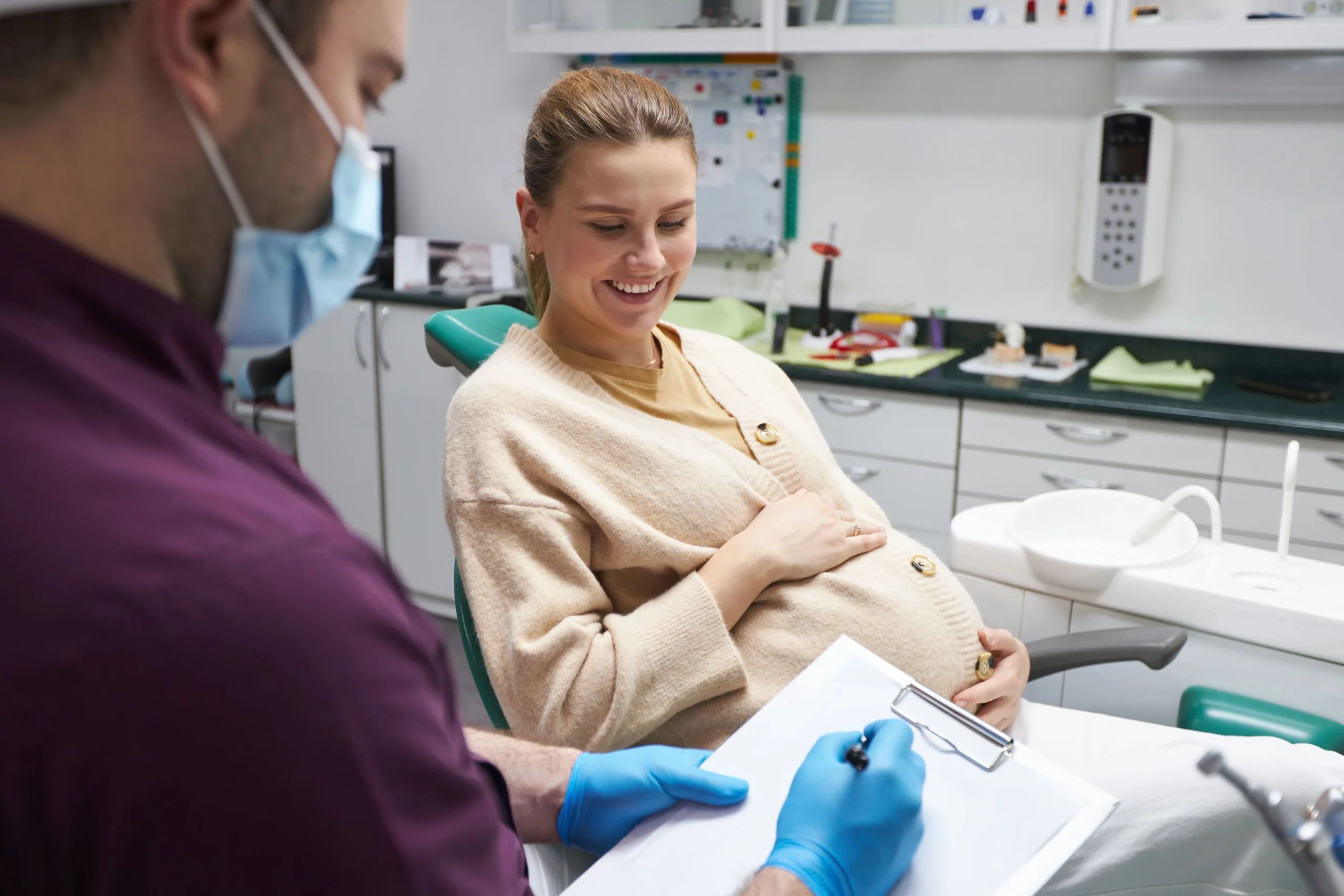 A happy pregnant woman on the dentist chair smiling while the dentist shows her a chart